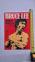 Front cover of Bruce Lee King of Kung-Fu book with a red background and image of Bruce Lee in martial arts pose alongside ruler showing size.