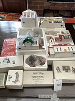 Overview of 11-piece Department 56 Snow Village set with original white styrofoam packaging, buildings with wired light elements, the Village Sounds cassette tape, and speakers.