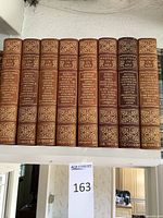 Front view of 10 volumes of Masters in Art antique book set on shelf showing brown leather spines with gold embossed designs and artists' names.