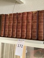 Photo showing 10 antique hardcover volumes titled Works of Thackeray with reddish-brown spine and gold decorations.