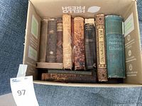 Overhead photo of box containing 9 antique books showing variety in binding and condition