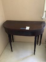 Antique dark wood half-oval drop-leaf table with turned legs and casters.