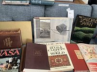 Books laid out on a couch, showing covers of The New American Bible, Complete Illustrated Rugs & Carpets of the World, Life's Pictorial History of World War II, The Gardens of Japan, and additional books.