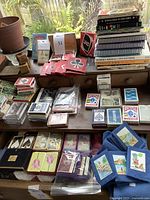 Overview photo showing dozens of decks of cards, books on card games and bridge, tally books, card game sets like Uno, and card-themed accessories including pouches and wooden blocks.