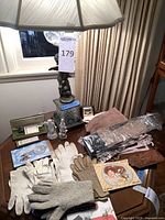 Photo showing Cherub lamp, multiple vintage gloves in fabric and knit, eyeglass case, glass statues, pen set, and decor arranged on a wooden table near window.