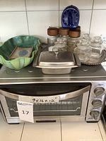 Wide shot showing all items on countertop including Cuisinart toaster oven, green ceramic dish, metal covered dish, ornate tray with salt and pepper shakers and jars, kitchen timer, and sushi plate.