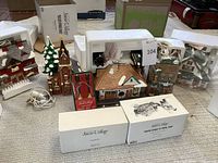 Overview of all eight Snow Village Christmas decorations with original packaging and electrical cords, laid out on floor.
