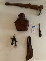 Full view of the wall display showing carved wooden hanging piece, woven container, buffalo bell and smaller artifacts.