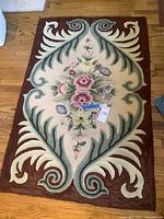 Full view of rectangular floral area rug with central bouquet and decorative border on hardwood floor.