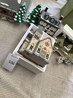 Four Snow Village brand light up Christmas houses shown together with white foam packaging around Redeemer Church house