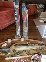 Photo showing two tall wooden carved figures with colorful Indigenous designs, standing on a wooden floor.