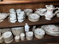 Full view of china set on wooden shelves showing cups, plates, serving dishes, with pink floral and gold trim pattern.