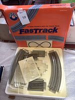 Original orange box with Lionel branding and product details, labeled 'Fig 8 Add-On Track Pack'. Contents laid out on tray include various curved and straight track pieces, connectors, and instruction manual.
