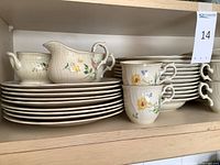 Shelf with Mikasa china dinner plates, serving pitchers, tea cups and saucers with floral designs.