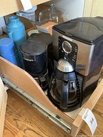Photo of Mr. Coffee machine, Cuisinart coffee maker, and Trudeau coffee thermoses placed on a wooden drawer shelf.