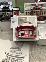 Photo showing the three ceramic Christmas village houses including the Harley-Davidson shop with motorcycle, Dyna's Drive-In diner, and Coca-Cola Bottling Plant. Items are partially in their original packaging with visible electrical cords.