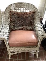 Front view of white wicker rocking chair with brown faux leather seat cushion and Persian rug pillow.