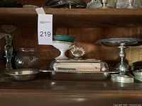 Photo showing silver plated cover dish, small dish, raised pedestal dish, and coasters on wooden shelf