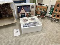 Various angles showing the ceramic buildings Big Bill's Service Station, Al's TV Shop, Toy Shop, and 2101 Maple, some in original styrofoam and boxes, with electrical cords.