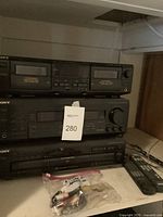 Full view of the stacked three components of the Sony sound system on a shelf with a lot tag number 280.
