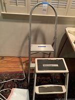 Two stepstools side by side, aluminum stepstool with handrail behind metal stepstool.