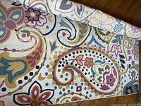 Close-up of rolled edge showing colorful floral and paisley pattern on cream background.