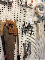 Pegboard with wooden-handled saws, pliers, cutters, and hammer hung on hooks.