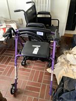 Photo showing black wheelchair parked behind purple walker on tiled floor, highlighting size and condition