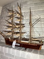 Full side view of wooden ship model with three masts, beige sails, detailed rigging, and brown hull with painted circular accents.