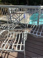 Set of three wrought iron patio chairs on a wooden deck near a pool, showing wear, chipped paint, and missing cushions