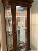 Front view of wooden curio cabinet showing curved glass front and interior shelves.