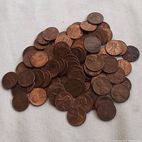 Pile of approximately 90 US pennies showing both heads and tails with Abraham Lincoln on the obverse and the Lincoln Memorial on the reverse.