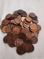 Pile of approximately 85 USA pennies showing both obverse and reverse faces, mostly copper-colored with Lincoln Memorial design on reverse.
