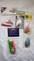 Five fishing lures arranged on white background showing packaged DFS lure, ProChip 4 Flasher lure, and various metal and painted lures