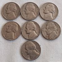 Seven 1970s US 5 cent coins (nickels) laid out on a white cloth showing obverse side with Thomas Jefferson profile.
