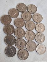 Top-down image of 18 US 5 cent coins showing obverse and reverse sides in various conditions spread out on white surface.