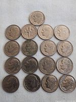 Top-down view of 16 US dimes arranged in rows on white cloth, showing the obverse side with Roosevelt's profile.