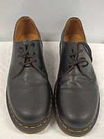 Front view of black leather Dr. Martens shoes showing toe area with slight creases and yellow stitching on sole.
