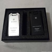 Photo of the audio transmitter and receiver side by side in foam case, showing front labels and indicator lights.