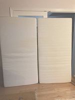 Two IKEA foam mattresses standing upright side by side, showing full front view with clean white fabric covers.