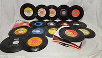 Collection of 17 45 RPM vinyl records laid out, showing records and some paper sleeves.
