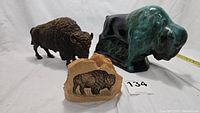 Three bison items shown side by side on a white surface: Blue Mountain Pottery glazed bison, dark metal bison figurine, and beige resin rock engraved with bison image.