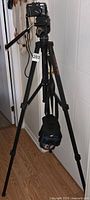 Canon PowerShot G2 camera mounted on black Phototec Video-900 tripod shown fully extended on wooden floor.