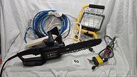 Photo of Remington electric chainsaw, extension cords, heavy duty lock and security cable, Designers Edge worklight displayed against white background.