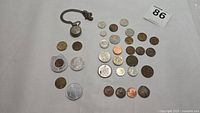 Multiple vintage coins and a coin necklace laid out on white surface. Various coins including Canadian penny, farthings, fifty cent pieces, and others.