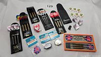 Overview of three dart sets and accessories including flights and tips arranged on cloth background.