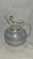 Front view of the round glass pitcher showing the sugar-frosted blue middle section and gold stripes.