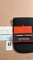 Mechanical pencil and pen set with refill cartridge and black metal case with orange insert, along with instruction cards.