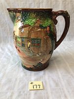 Front side of jug showing detailed village cottage and a figure at the window amidst tree foliage.