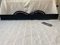 Front view of VIZIO sound bar with black fabric grille and included remote control placed on white surface.